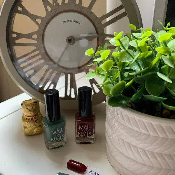 Two nail polish bottles with a small teddy bear and plant in the background.
