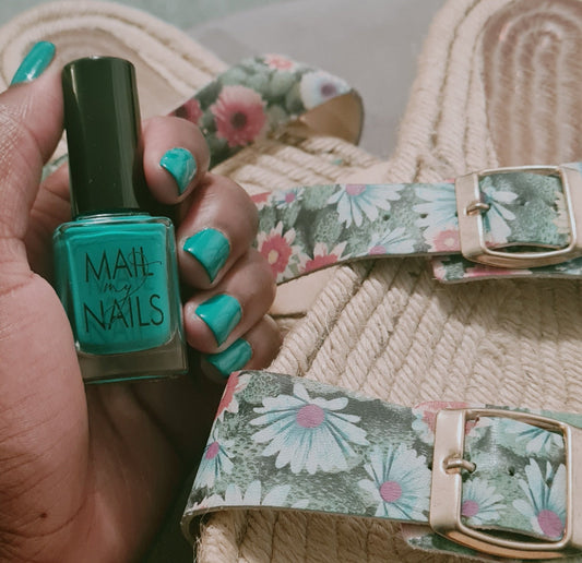 Swatch of emerald green nail polish on nails, near sandals