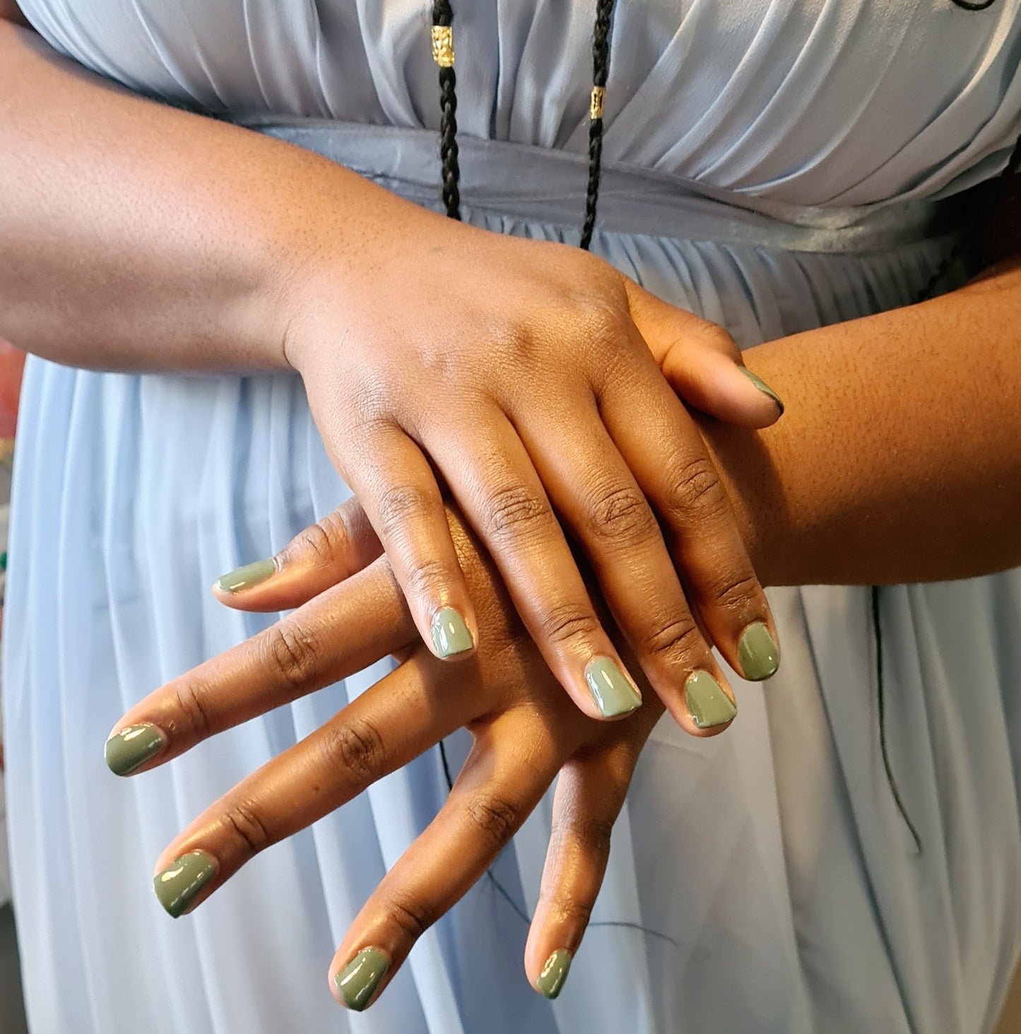 Swatch of olive green nail polish on nails, against bridesmaid dress