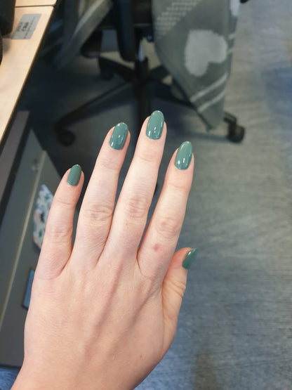 Swatch of olive green nail polish on nails, in the workplace