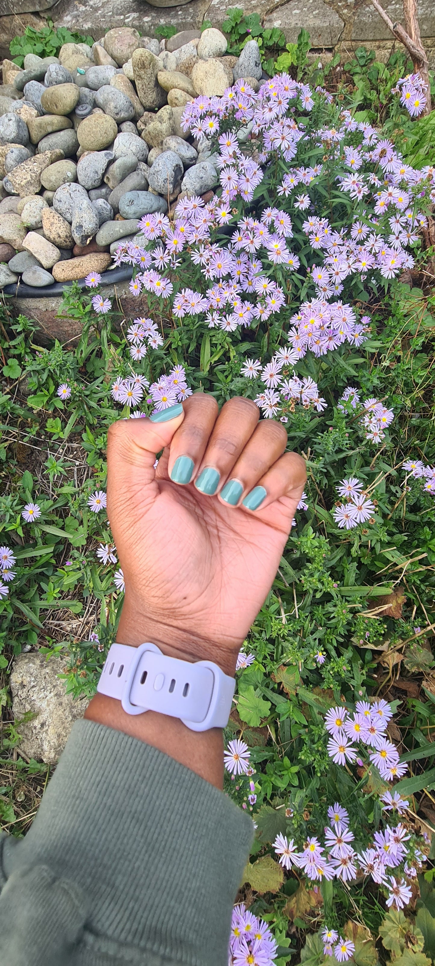 Swatch of olive green nail polish on nails, around flowers.