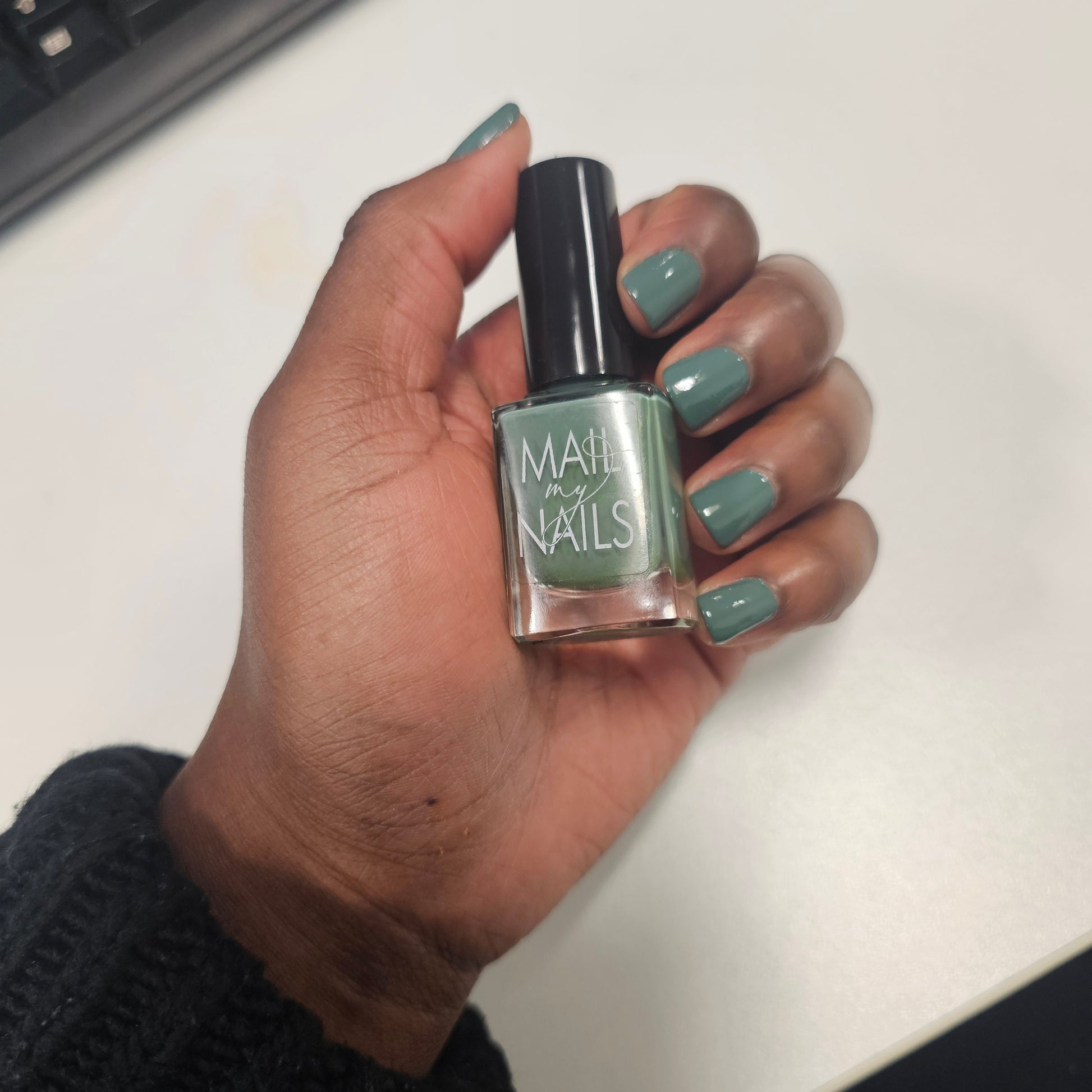 Swatch of olive green nail polish on nails, in the office.